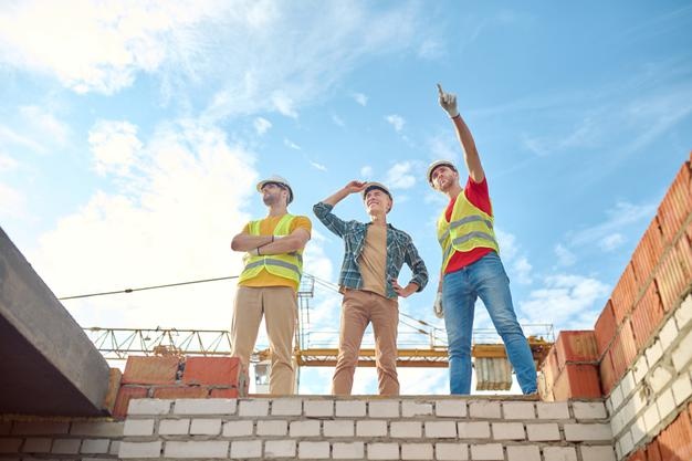 Men standing on brick wall of building under construction Free Photo